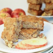 Apple Nut Brownies shown on a stack of white plates with apples on the side.