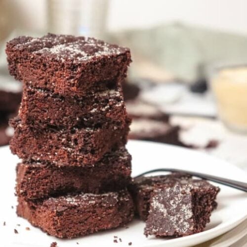 Keto Peppermint Brownies shown stacked on a white plate with fork in the background.