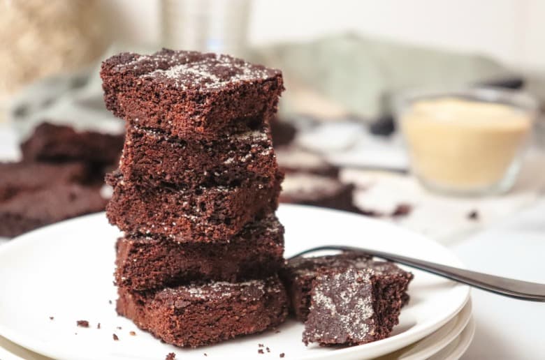 Keto Peppermint Brownies shown stacked on a white plate with fork in the background.