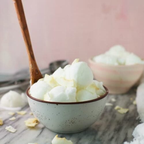 Coconut Ice Cream shown in a bowl with a wooden spoon on a marble table.