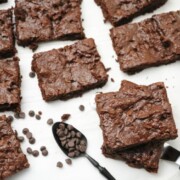 Paleo Chocolate Chip Brownies Recipe shown cut on parchment paper with spoon and chocolate chips around it.