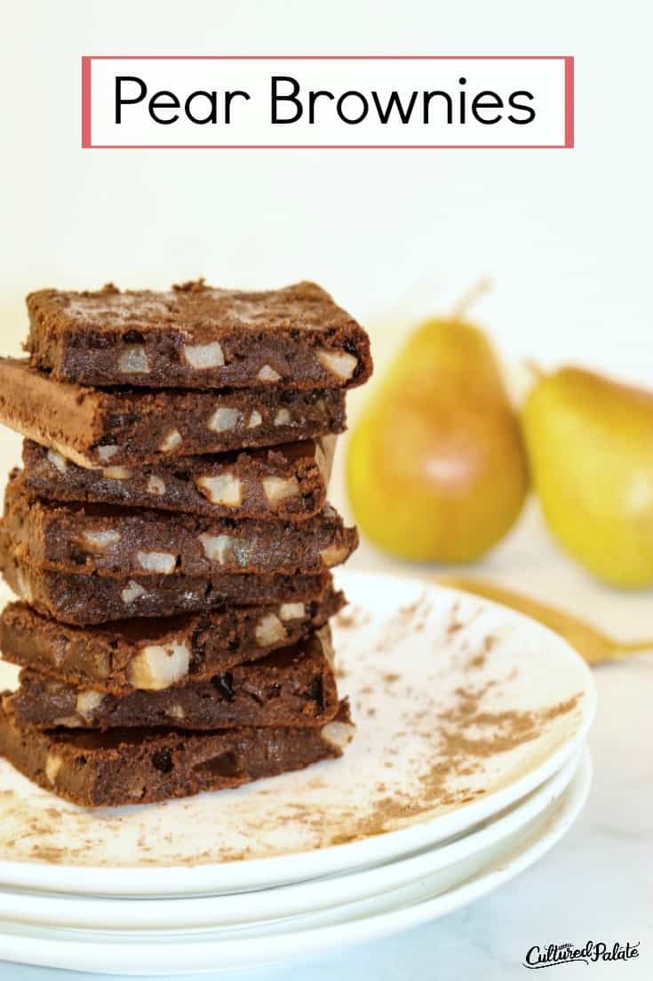 Pear brownies shown stacked on a white plate with pears in the background