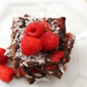 Raspberry Coconut Brownies shown on glass plate with fresh raspberries on top.