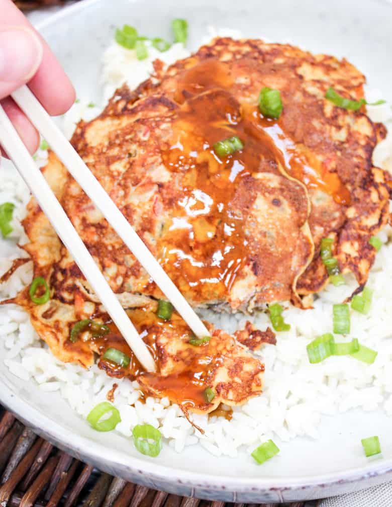 Egg Foo Young pancakes over rice in a bowl with gravy and eaten with chopsticks